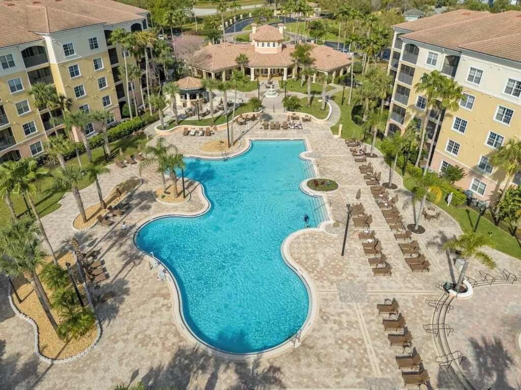 A resort with a central swimming pool, multiple guest buildings, and palm trees.