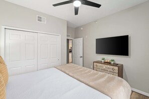 A bedroom with a bed, a ceiling fan, a TV mounted on the wall, and a door leading to another room. - Modern Disney Escape, Near the Parks (Orlando)
