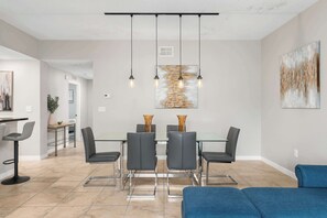A modern dining area with a glass table, four chairs, and pendant lighting. - Modern Disney Escape, Near the Parks (Orlando)