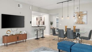 Uma sala de estar moderna com uma TV de tela plana, um console de madeira e uma área de jantar com uma mesa e cadeiras de vidro.