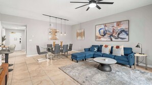 Uma sala moderna com um sofá seccional, um espaço de jantar com mesa de vidro e um ventilador de teto.