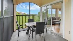 Ein überdachter Patio-Bereich mit Tisch und Stühlen, eine Glastür, die zu einem Wohnbereich führt, und Blick auf eine grüne Landschaft.
