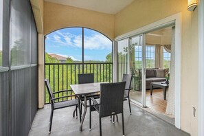 Ein überdachter Patio-Bereich mit Tisch und Stühlen, eine Glastür, die zu einem Wohnbereich führt, und Blick auf eine grüne Landschaft.