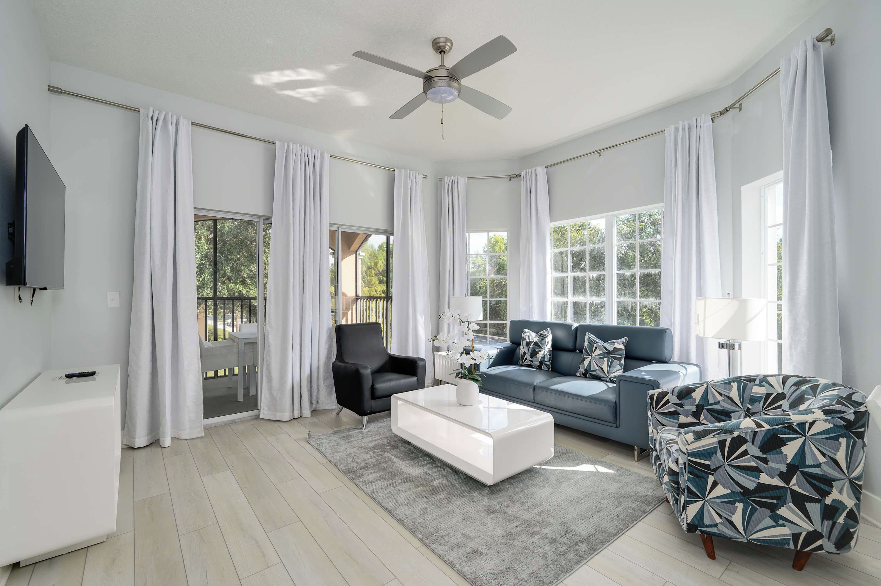 Una sala de estar moderna con ventilador de techo, un sofá, una mesita de centro y un sillón estampado.