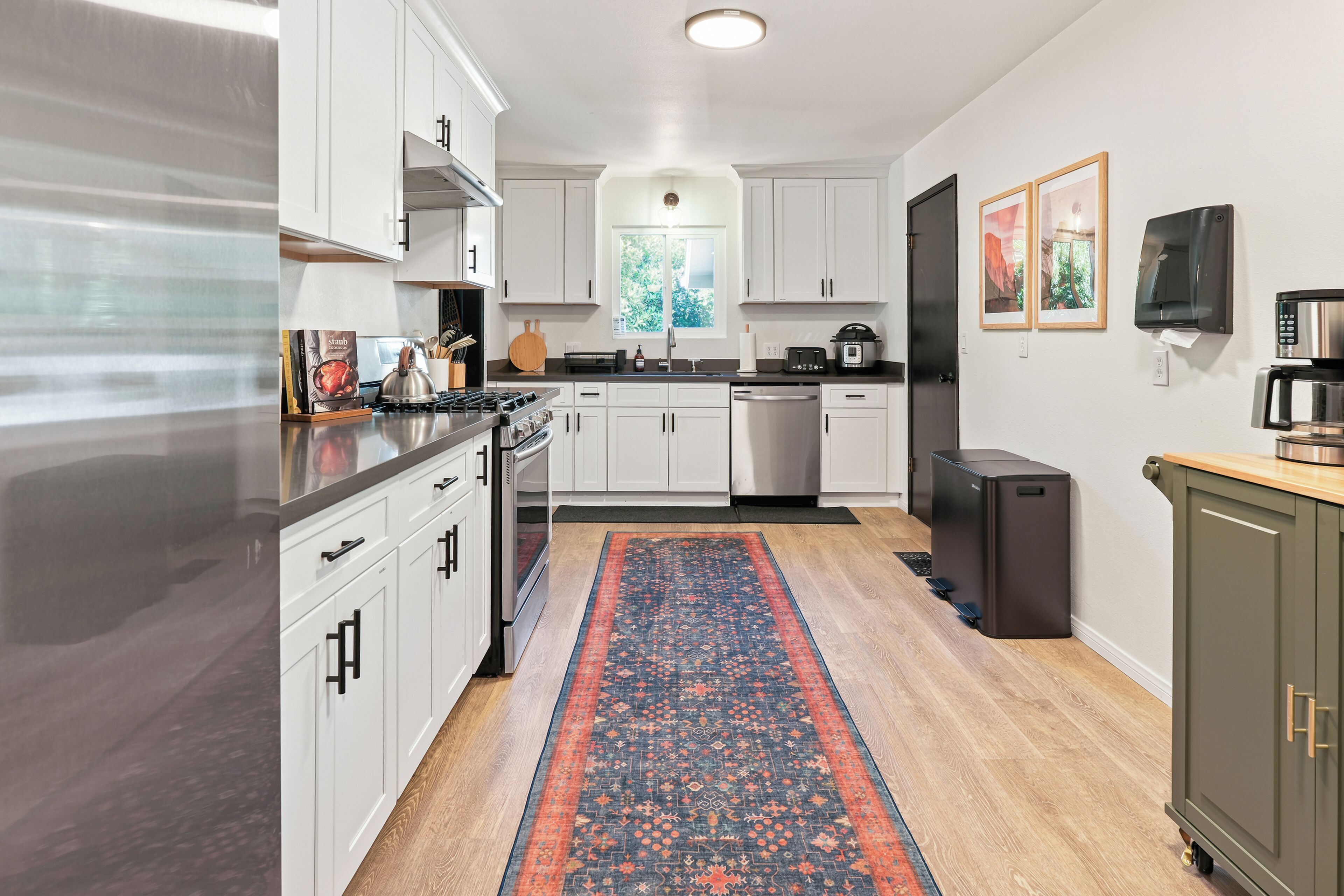 Une cuisine moderne avec des meubles blancs, des appareils en acier inoxydable et un tapis à motifs.