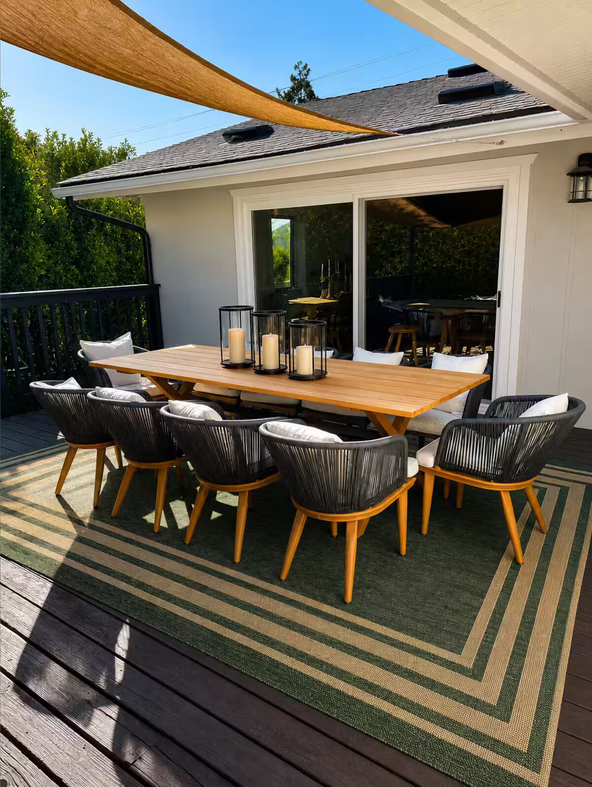 An outdoor patio with a wooden table and chairs, surrounded by a green and beige striped rug.