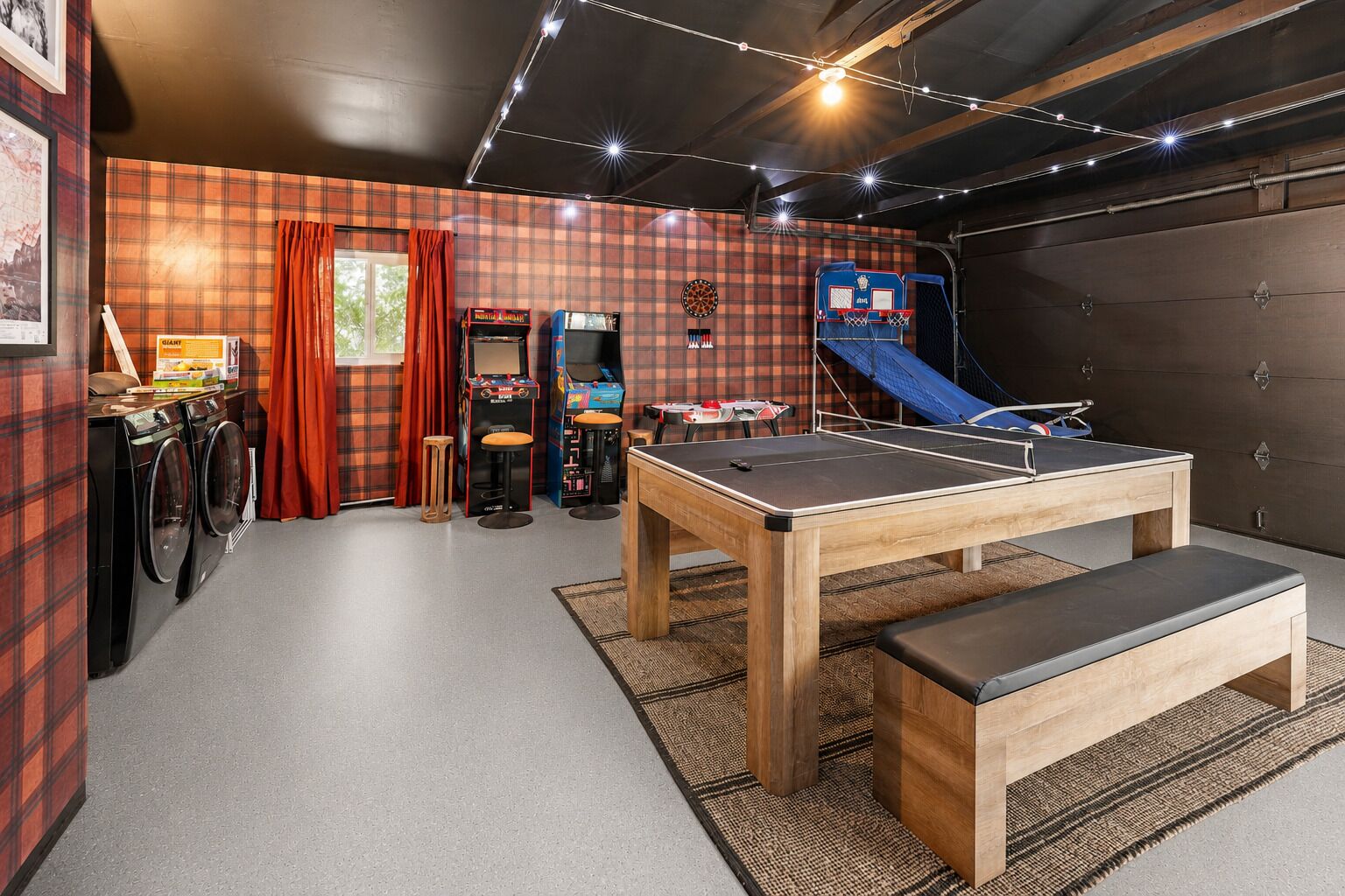 A room with a ping pong table, a dartboard, arcade games, and a blue slide.