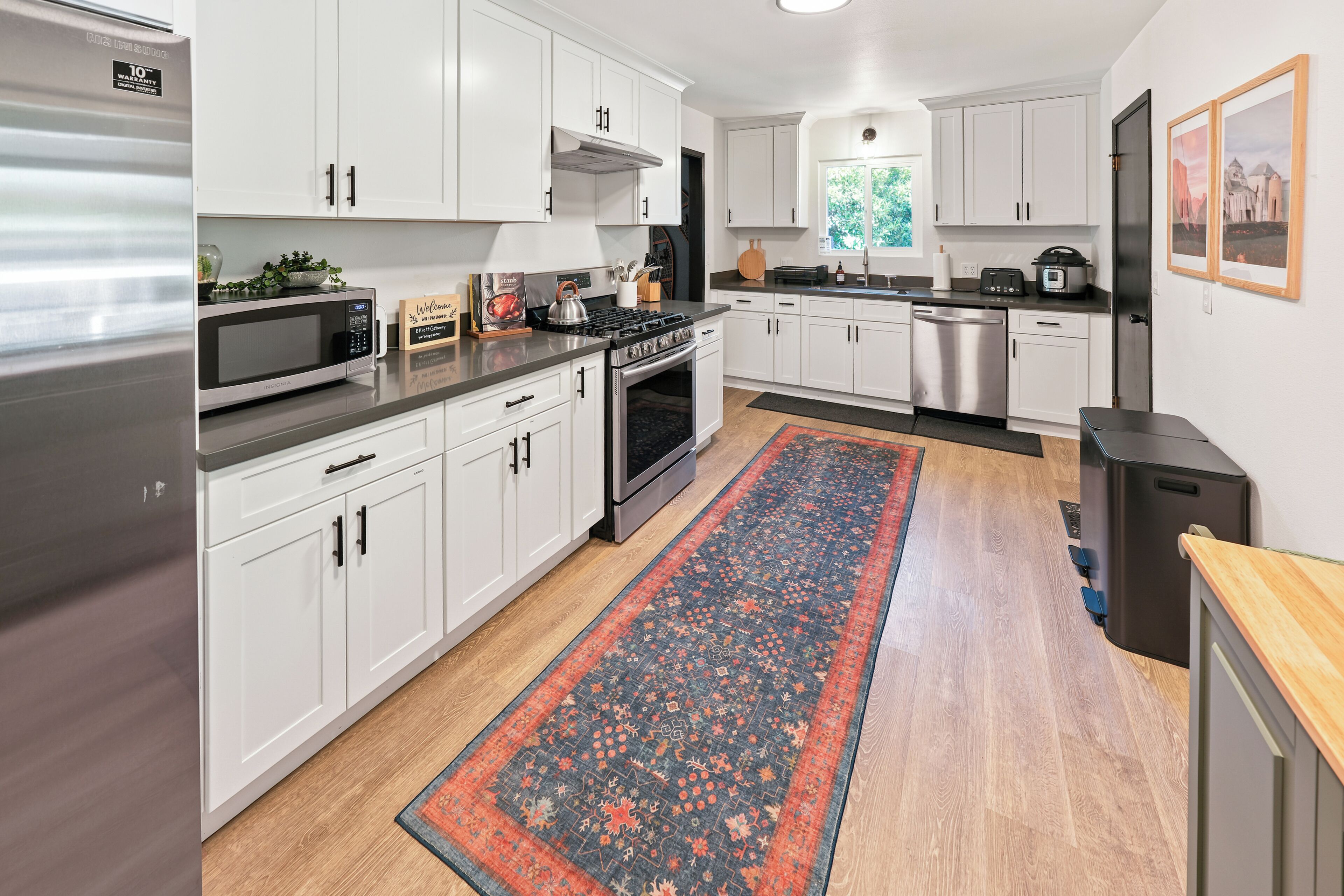 A modern kitchen with stainless steel appliances, white cabinetry, and a decorative rug.