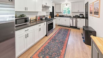 A modern kitchen with stainless steel appliances, white cabinetry, and a decorative rug.
