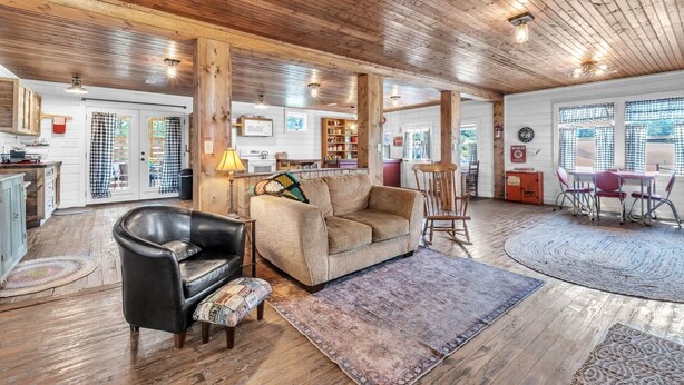 Ein gemütliches Interieur mit Holzbalkendecke, einer Couch, einem Ledersessel und einer Essecke mit Tisch und Stühlen.