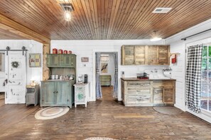 A rustic kitchen with wooden cabinets, a coffee machine, and a view of the outdoors through a window. - The Country Store at Clemson (Anderson County)