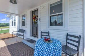 A porch with a checkered tablecloth, two chairs, a red bucket, and a bottle of soda. - The Country Store at Clemson (Anderson County)