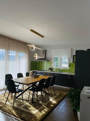 A modern kitchen with a dining area, featuring a large table, chairs, and a hanging light fixture. - 3 bedroom and 2 bathrooms apartment in Anatoli area with AC for relaxing stays (Anatoli)