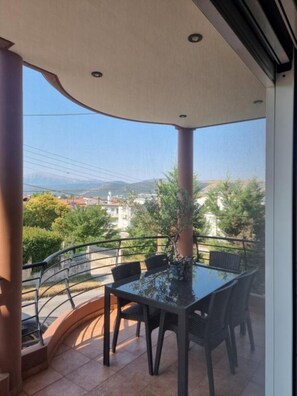 A balcony with a glass table and chairs, a view of a mountainous landscape, and a railing. - 3 bedroom and 2 bathrooms apartment in Anatoli area with AC for relaxing stays (Anatoli)