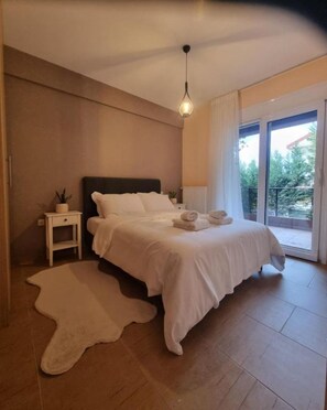 A bedroom with a bed, bedside tables, a hanging light fixture, and a view through a glass door. - 3 bedroom and 2 bathrooms apartment in Anatoli area with AC for relaxing stays (Anatoli)