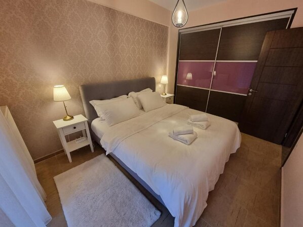 A bedroom with a bed, bedside lamps, a nightstand, a door, and a white rug. - 3 bedroom and 2 bathrooms apartment in Anatoli area with AC for relaxing stays (Anatoli)