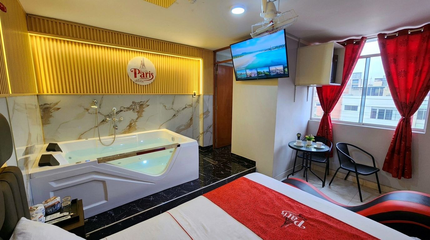 A hotel room with a large bathtub, a television, a small table with chairs, and a view of the city.