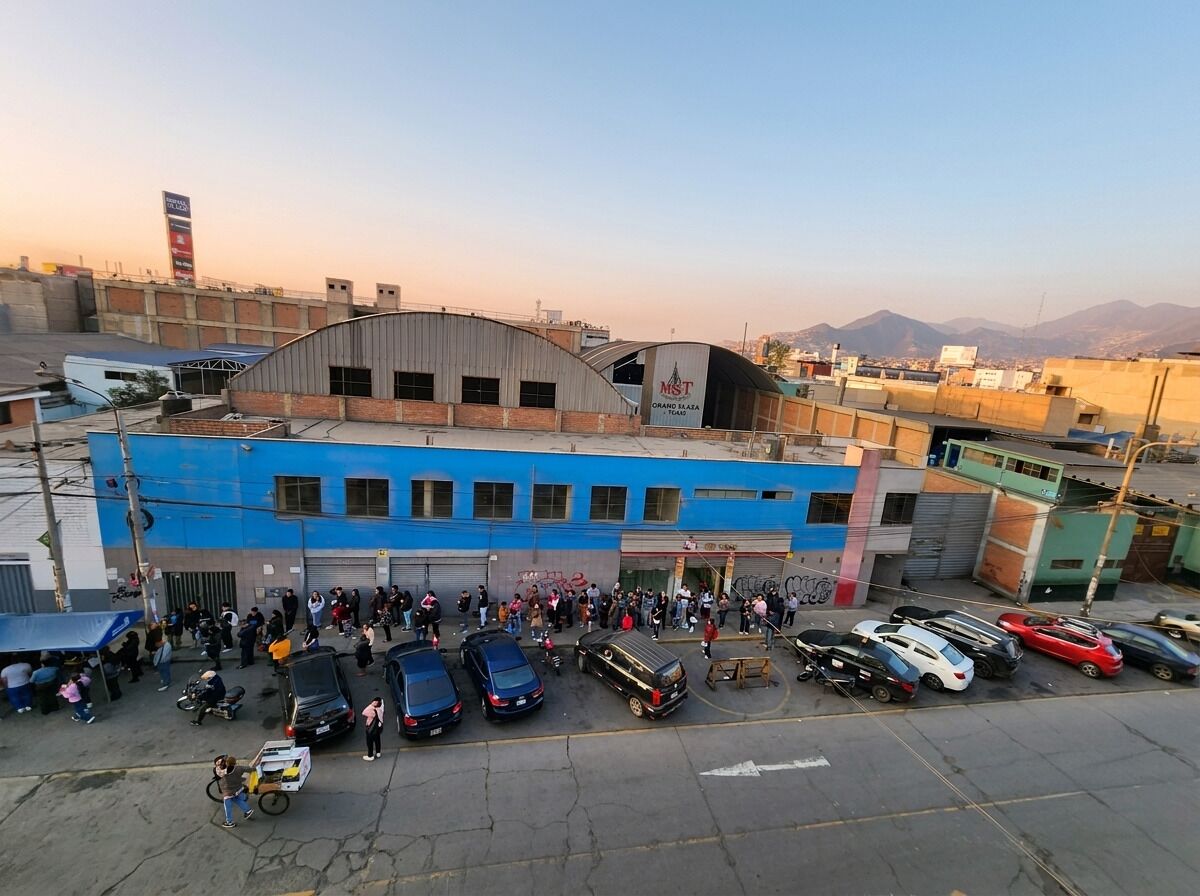 A building with a blue facade and a curved roof, surrounded by parked cars and a crowd of people.