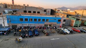 A building with a blue facade and a curved roof, surrounded by parked cars and a crowd of people.