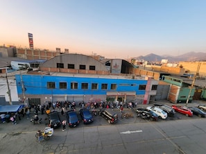 A building with a blue facade and a curved roof, surrounded by parked cars and a crowd of people.