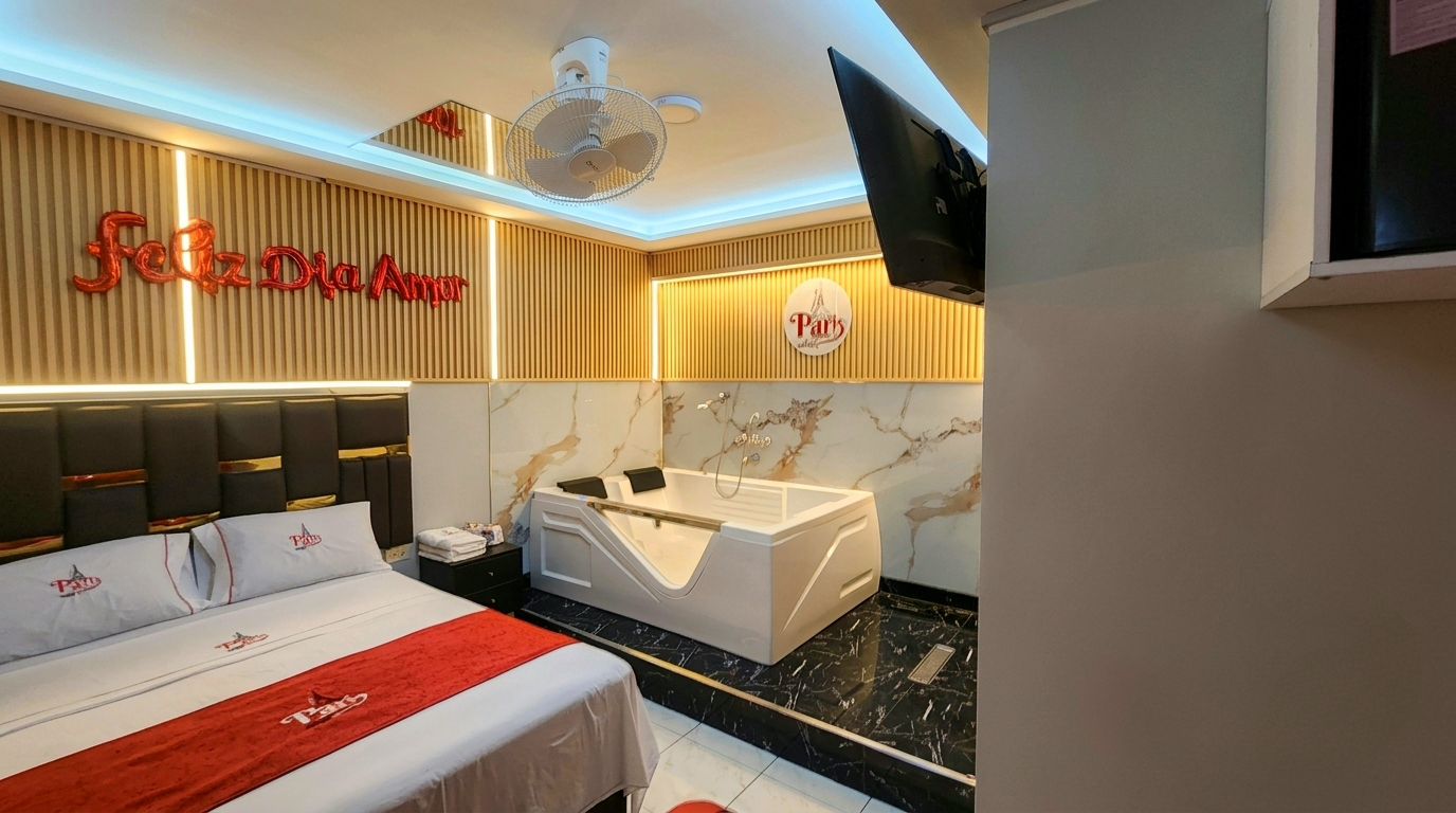 A hotel room with a bed, a bathtub, a TV, and a wall with a 'Feliz Dia Annor' sign.