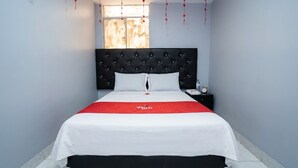A hotel room with a bed, a nightstand, a window, and a red bedspread.