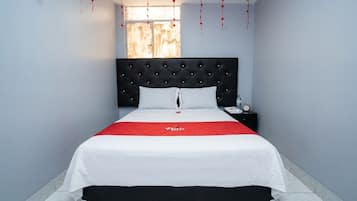 A hotel room with a bed, a nightstand, a window, and a red bedspread.