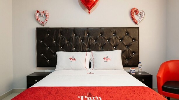 A hotel room with a bed, two nightstands, a red chair, and heart-shaped balloons on the wall.