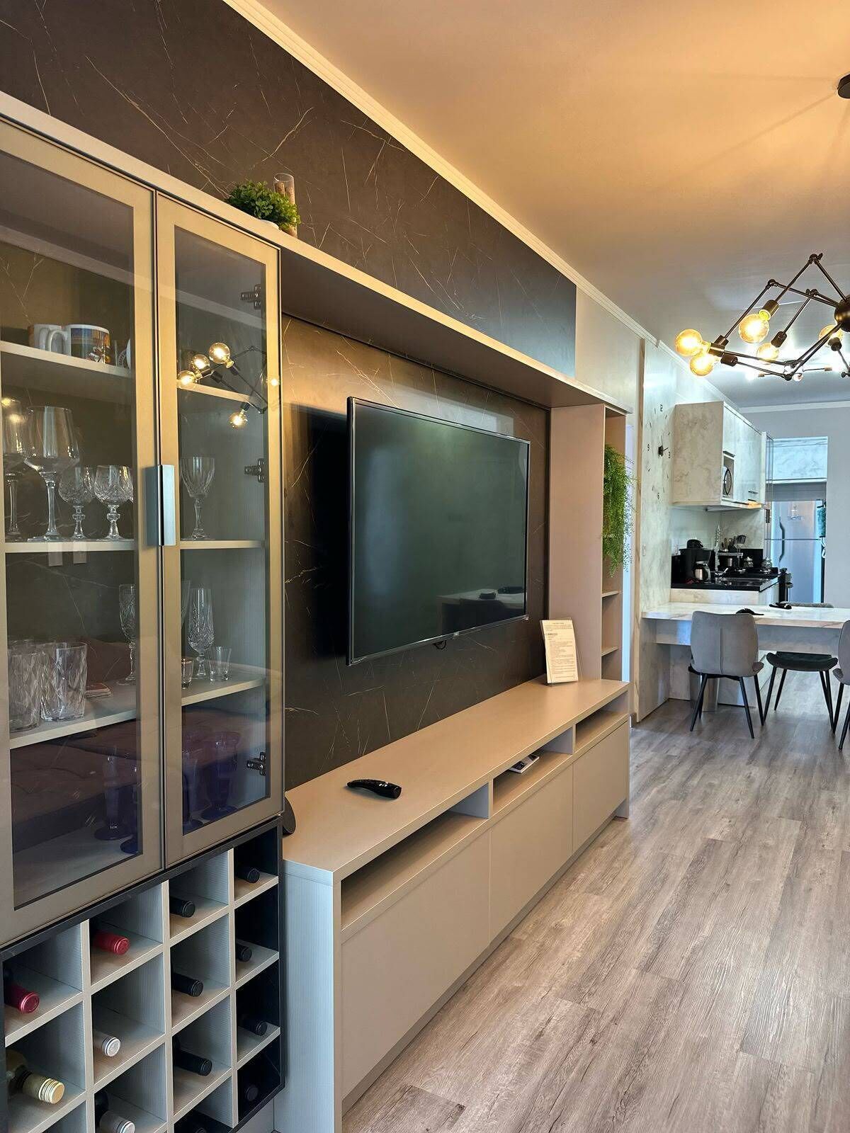 A modern living space with a built-in TV, wine storage, and a kitchen area.
