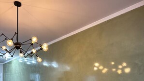 Ein stilvolles Wohnzimmer mit Ecksofa, einer Hängeleuchte und einer Wand mit strukturierter, grüner Oberfläche.