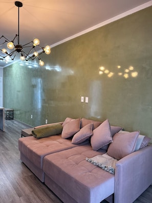 A modern living space with a sectional sofa, a hanging light fixture, and a green textured wall. - Apto Avenida principal Urubici (Urubici)