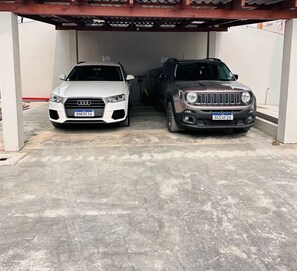 Two cars parked under a covered area with a concrete floor. - Apto Avenida principal Urubici (Urubici)