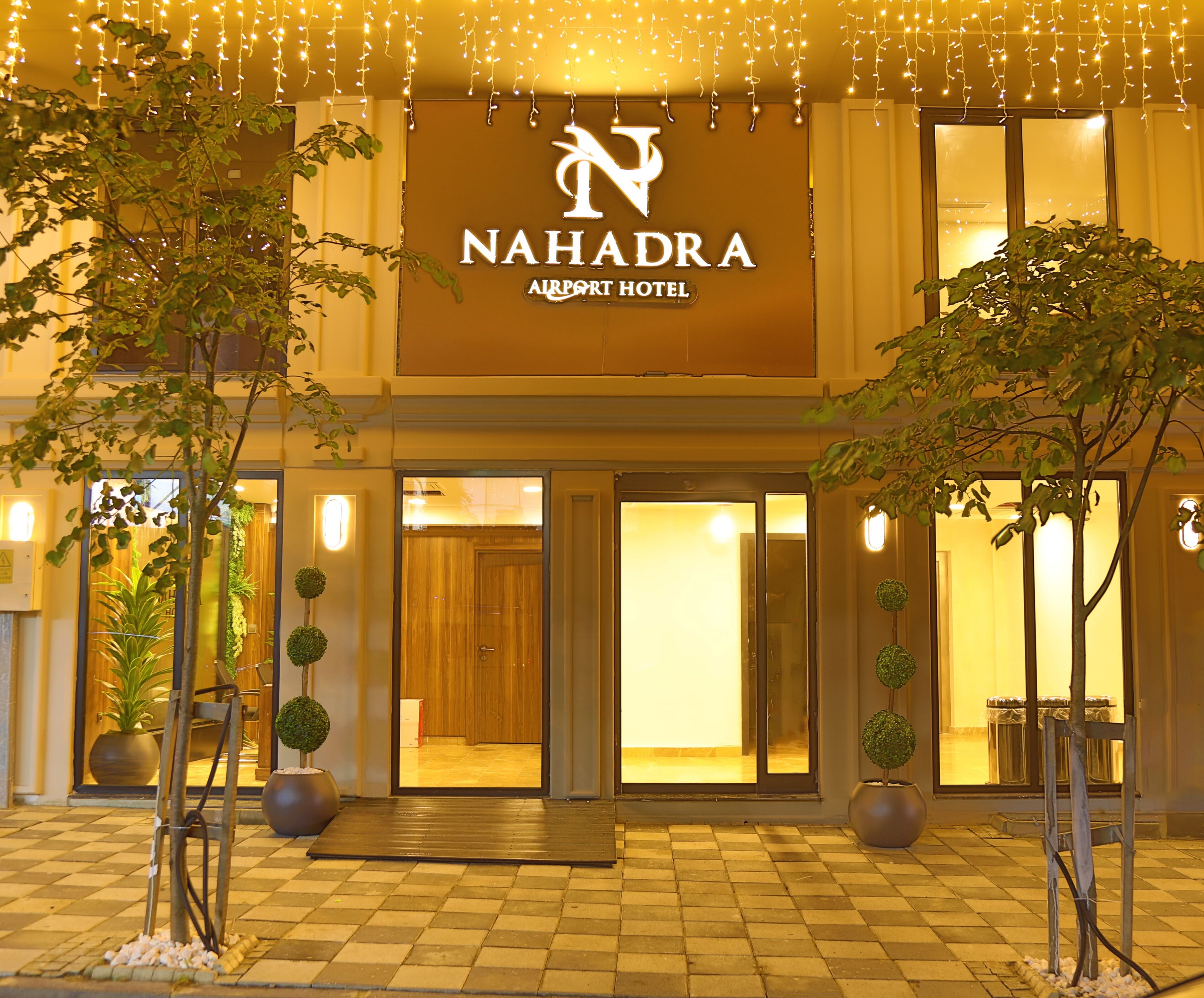 Exterior del Hotel Nahadra Airport, con entrada despejada, plantas en macetas y un cartel sobre las puertas.