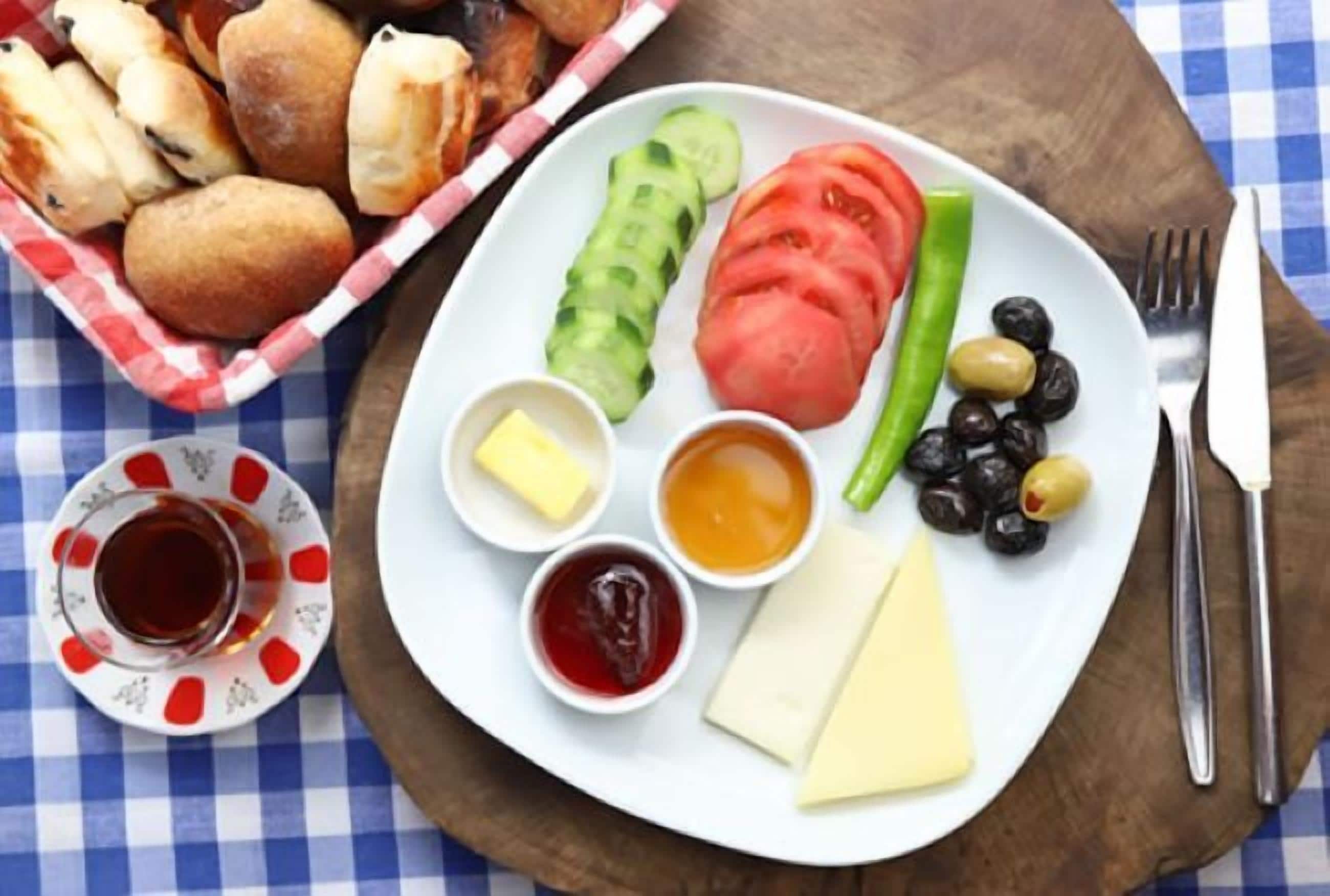 A plate with cheese, olives, tomatoes, and pickles, accompanied by a small bowl of jam and mustard.