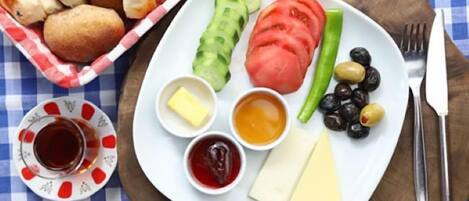 A plate with cheese, olives, tomatoes, and pickles, accompanied by a small bowl of jam and mustard.