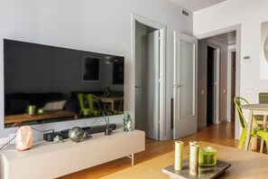Ein modernes Wohnzimmer mit großem Flachbildfernseher, einer weißen Unterhaltungsanlage mit Dekoration und einem Essbereich mit Tisch und Stühlen.