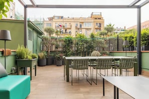 Eine Dachterrasse mit Tisch und Stühlen, umgeben von Topfpflanzen und Blick auf Gebäude.