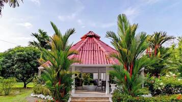 A gazebo with a red roof, surrounded by lush greenery and palm trees.