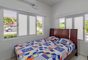 A bedroom with a bed, two windows, and a view of the outside.