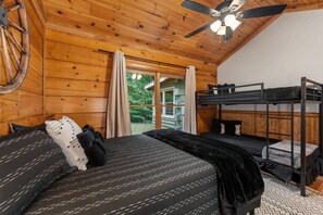 Ein Zimmer in einer Holzhütte mit einem Etagenbett, einem Deckenventilator und einem Fenster mit Vorhängen.