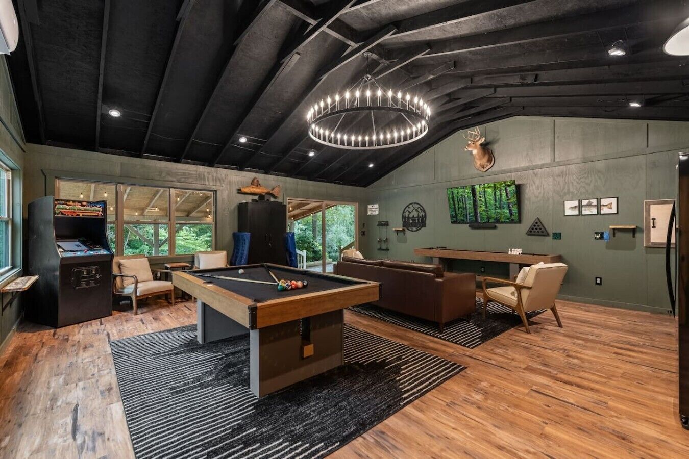 Une table de billard entourée de sièges, un poisson empaillé accroché au mur et une grande fenêtre donnant sur un paysage verdoyant.