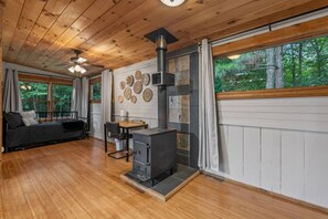 Interior acolhedor de uma cabana com teto de madeira, lareira, área de jantar e sofá.