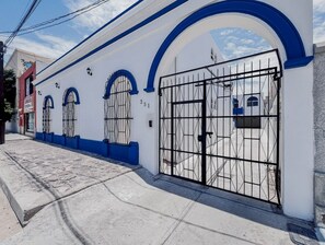 A building with a white facade and blue accents, featuring a large metal gate and arched windows. - Pichilingue Housing cerca del malecon (La Paz)