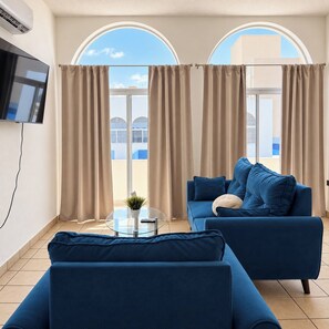 A modern living room with a blue sofa, a glass coffee table, and a flat-screen TV mounted on the wall. - Pichilingue Housing cerca del malecon (La Paz)