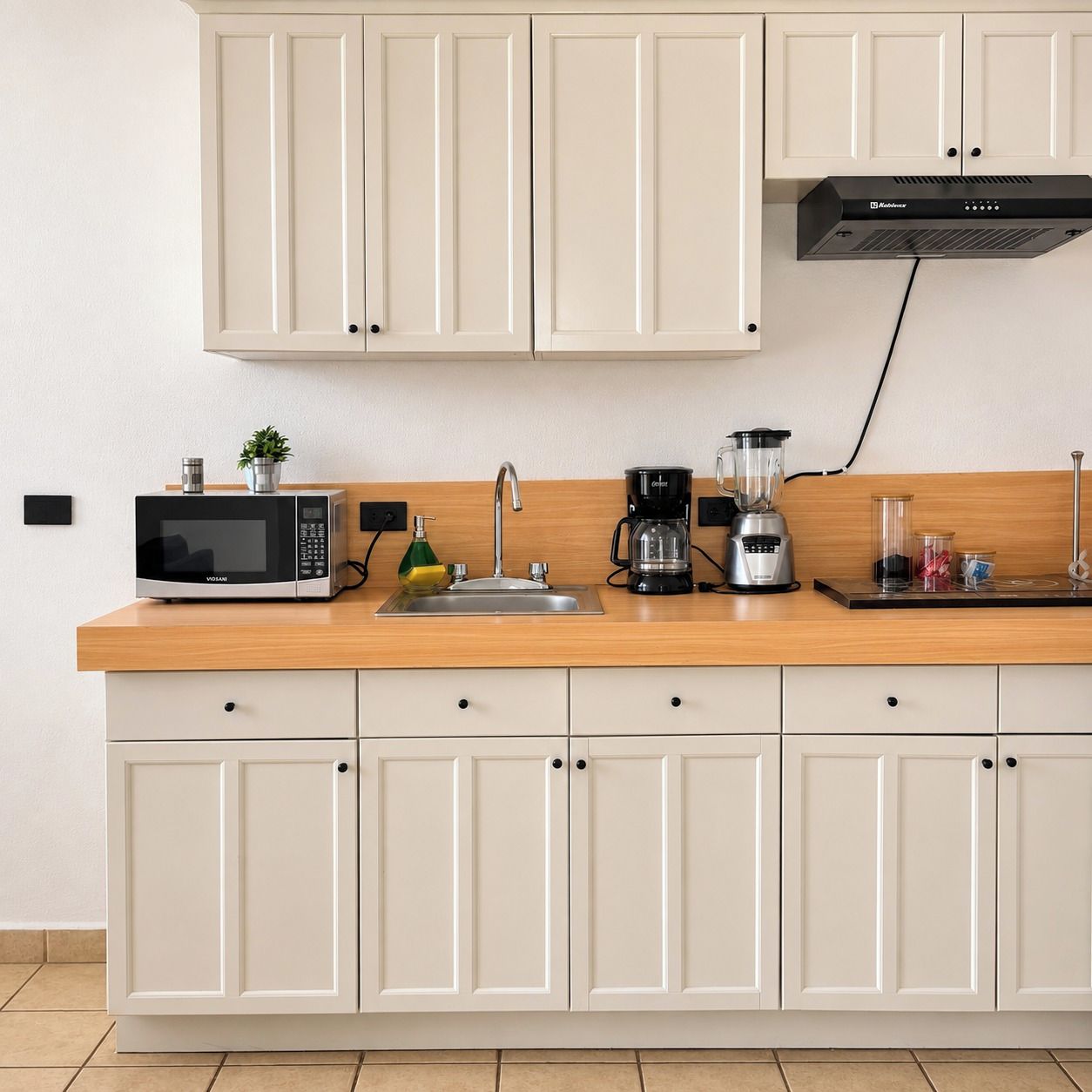 A kitchen with white cabinets, a wooden countertop, a microwave, a coffee maker, and a blender.