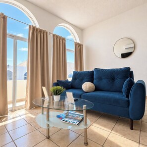 A modern living room with a blue sofa, a glass coffee table, and a view through large windows. - Pichilingue Housing cerca del malecon (La Paz)