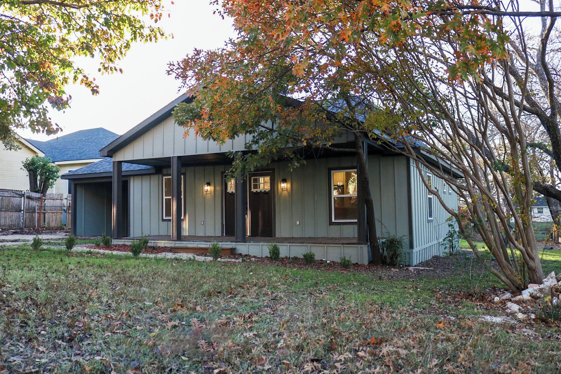 A single-story house with a porch, a small front yard, and a tree with autumn leaves.