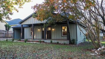 A single-story house with a porch, a small front yard, and a tree with autumn leaves.
