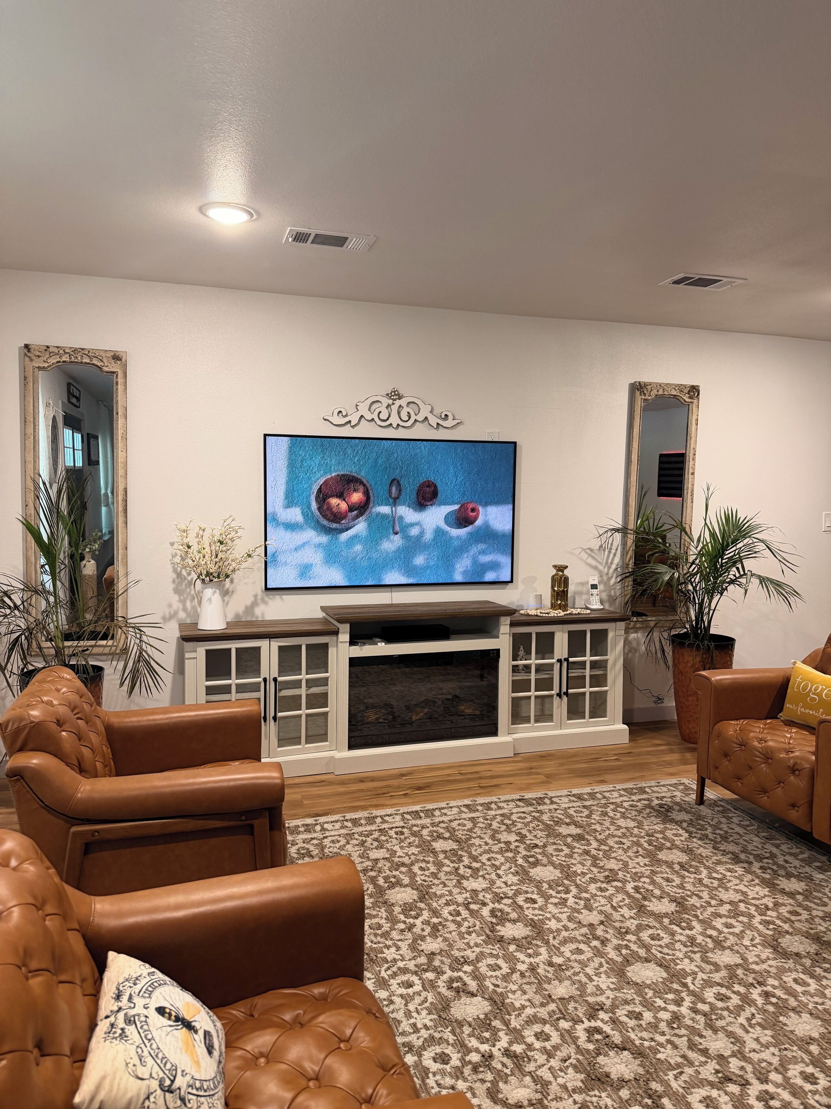 Een woonkamer met leren banken, een open haard, een televisie en decoratieve spiegels.