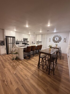 Una cocina moderna con armarios blancos, un refrigerador de acero inoxidable y un comedor con mobiliario de madera.